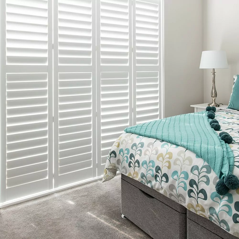 Bedroom blinds closed plantation shutters on bedroom window, with bed and lamp in view