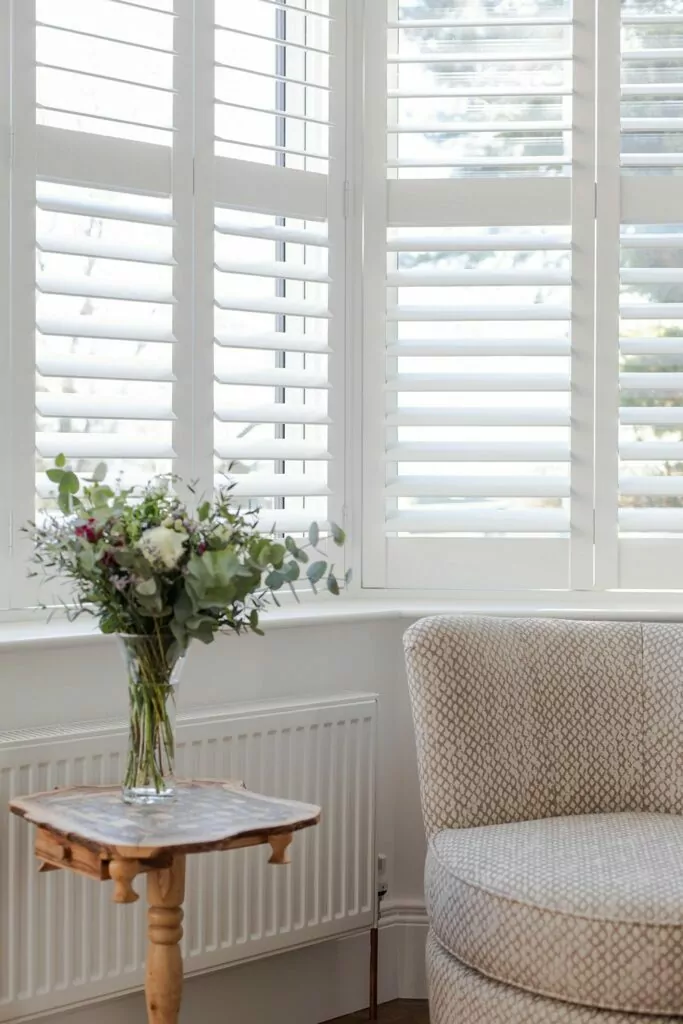 Plantation shutters in front of table with flowers and chair